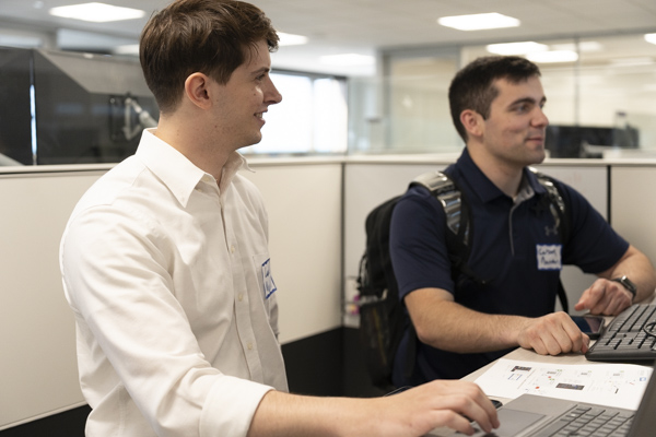 Two employees collaborating at a desk with their laptops