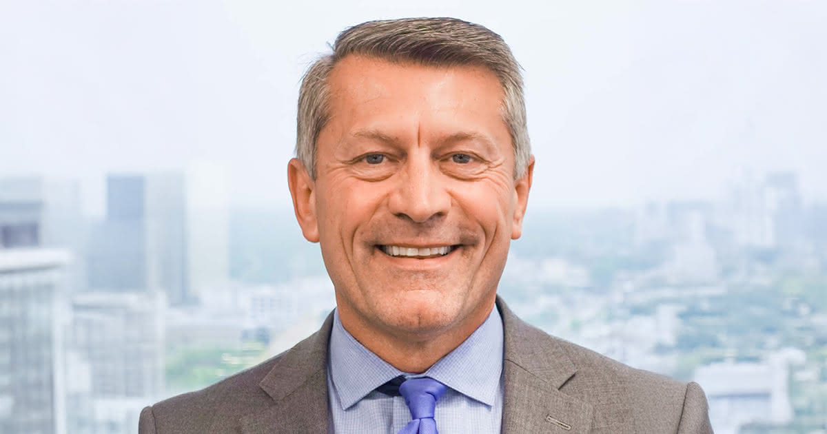 Ron Barrett smiling in front of a window showing the skyline of Des Moines Iowa